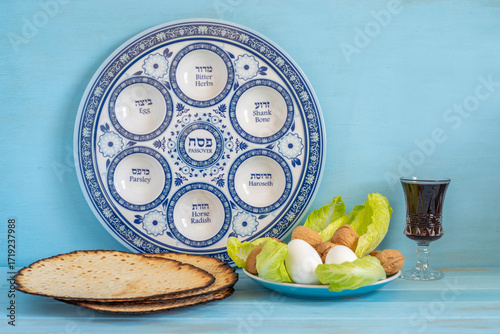 Jewish holiday Pesach or Passover background with Seder Plate and symbolic food eggs, lettuce, walnuts, matzah on blue wood. 

