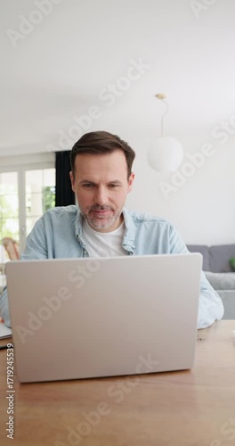 Vertical video of happy adult man opening laptop at home and using it