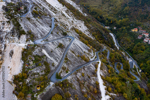Aerial view of winding road snaking through the stark white marble quarries, contrasting with the green vegetation, Carrara, Tuscany, Italy.