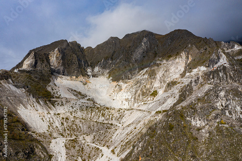 Aerial view of stark white marble quarries cascading down the rugged, textured slopes of the Apuan Alps under a moody sky, Carrara, Tuscany, Italy.