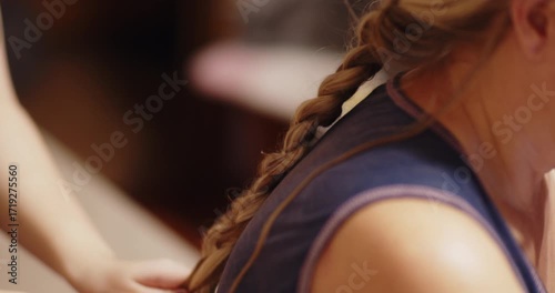 A girl learns to braid her mother's hair.