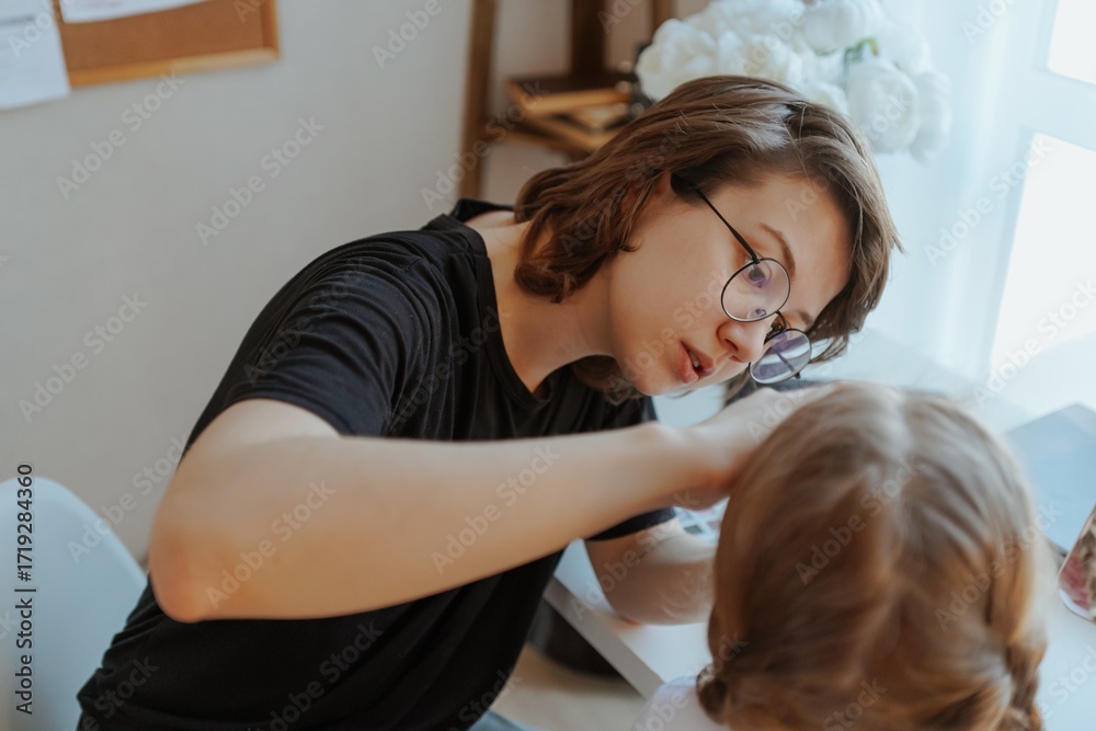 Fototapeta premium A young mother and her 3-year-old daughter play dress-up as makeup artists, sharing laughter and creativity. A heartwarming scene of role-playing, bonding, and joyful motherhood