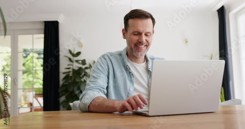 Video of smiling adult man opening and using laptop at home while sitting at table