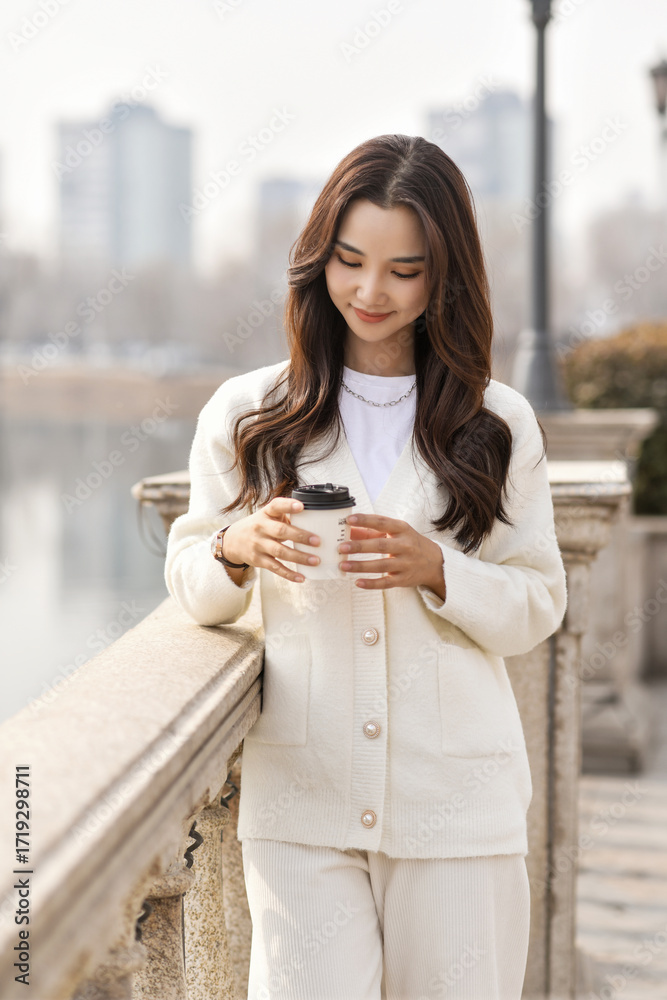 Fototapeta premium A young woman enjoying the scenery in the park, holding a coffee cup