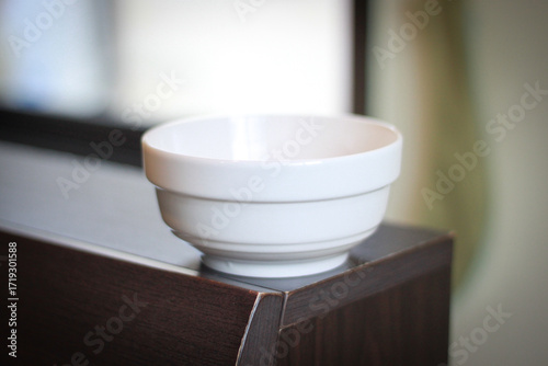 Bild auf Leinwand A clean white ceramic bowl placed on a wooden surface with natural light coming from the window