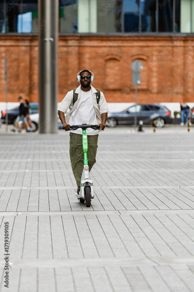 Obraz premium A male worker rides a scooter and listens in headphones
