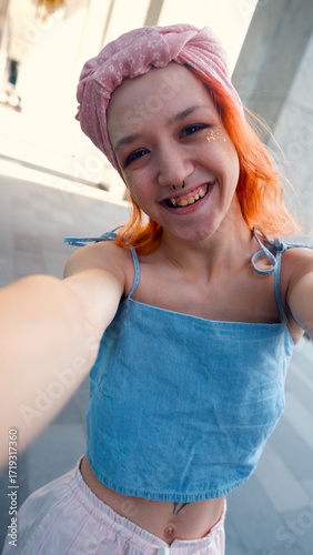 A teenage girl poses and smiles for a selfie on a smartphone.