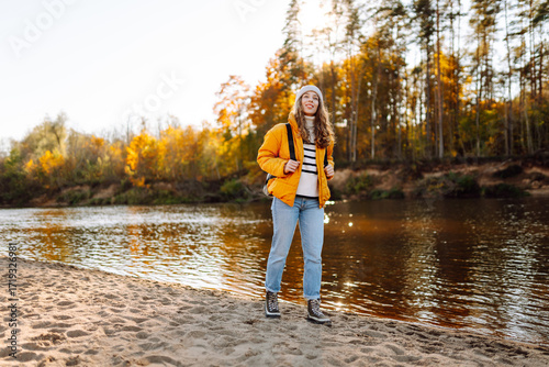 Εκτύπωση καμβά A beautiful hiker in a yellow jacket and carrying a backpack walks along a hiking trail along the river