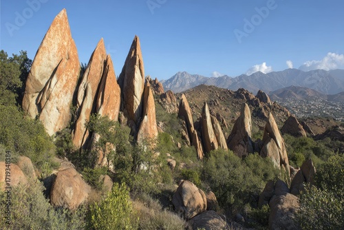 Rugged, reddish rock formations rise amidst scrubby hills under a clear sky