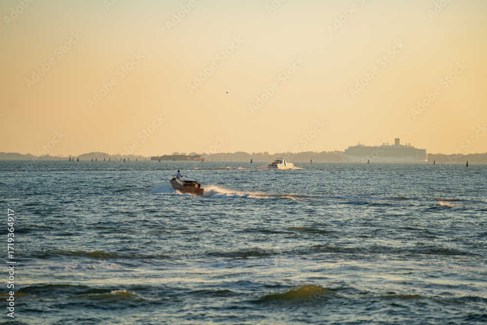 Fototapeta premium Speedboats crossing shimmering sea during golden sunset with distant horizon and glowing sky, representing travel, leisure, maritime transportation and summer coastal lifestyle
