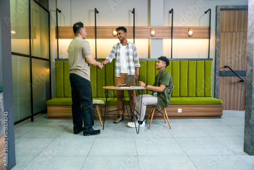 Three Asian Men Shaking Hands in Modern Coworking Space, Symbolizing Successful Business Partnership