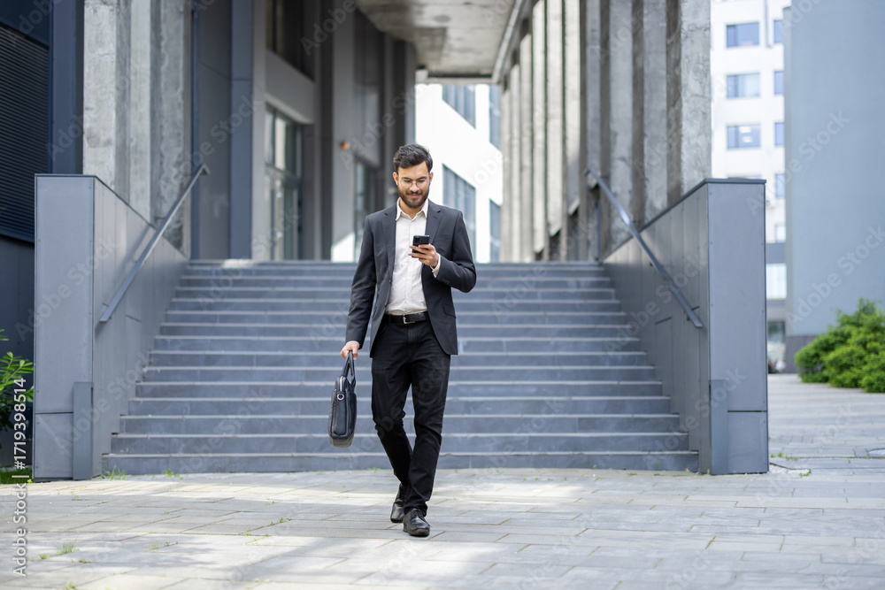 © Liubomir - Businessman walking down urban stairs using smartphone and carrying a briefcase, representing concepts of modern communication, business travel, and technology integration