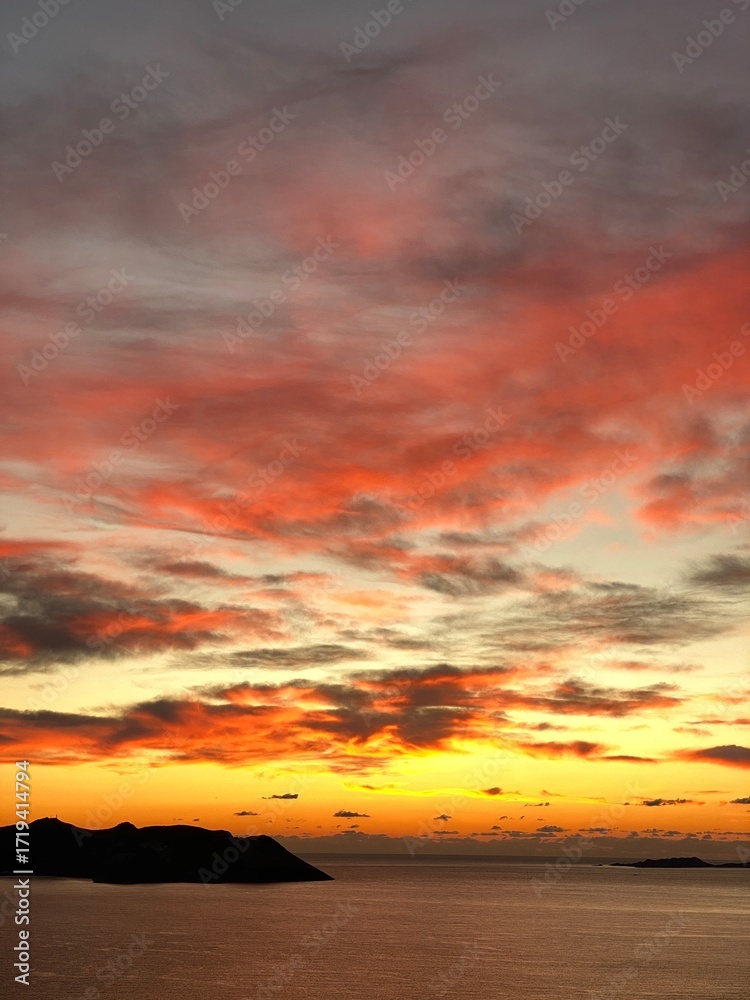 Fototapeta premium Vibrant sunset sky over ocean with dramatic clouds and silhouettes, ideal for background