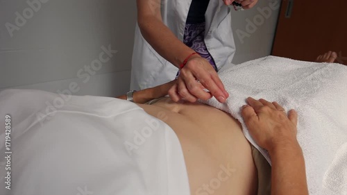 Traditional chinese medicine specialist inserting acupuncture needles into a patient's abdomen during a therapy session to stimulate energy flow and promote healing in a wellness clinic