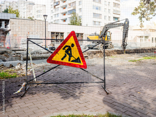 Digging works on streets with caution signs for people walking around with the excavator digging on the background