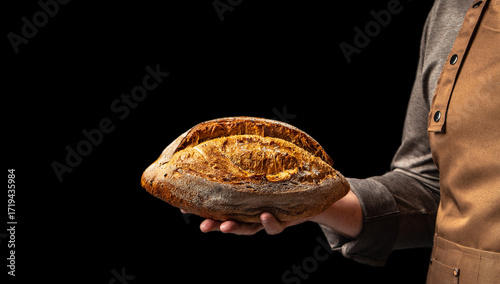 Foto Baker holding freshly baked rustic bread loaf on black background, close up, cop