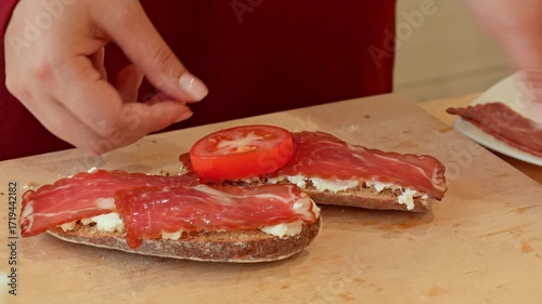 Female hands putting tomato slices on a bread during sandwich cooking close up