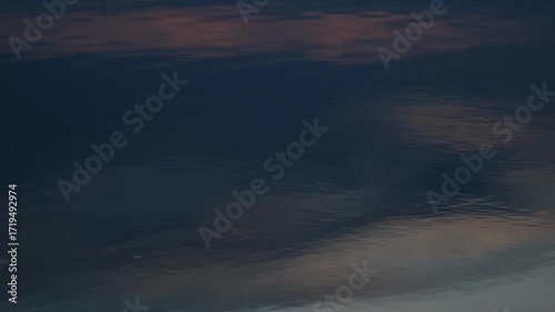 Reflective dark water surface with subtle ripples and abstract sky reflections changing over time, tranquil background footage.