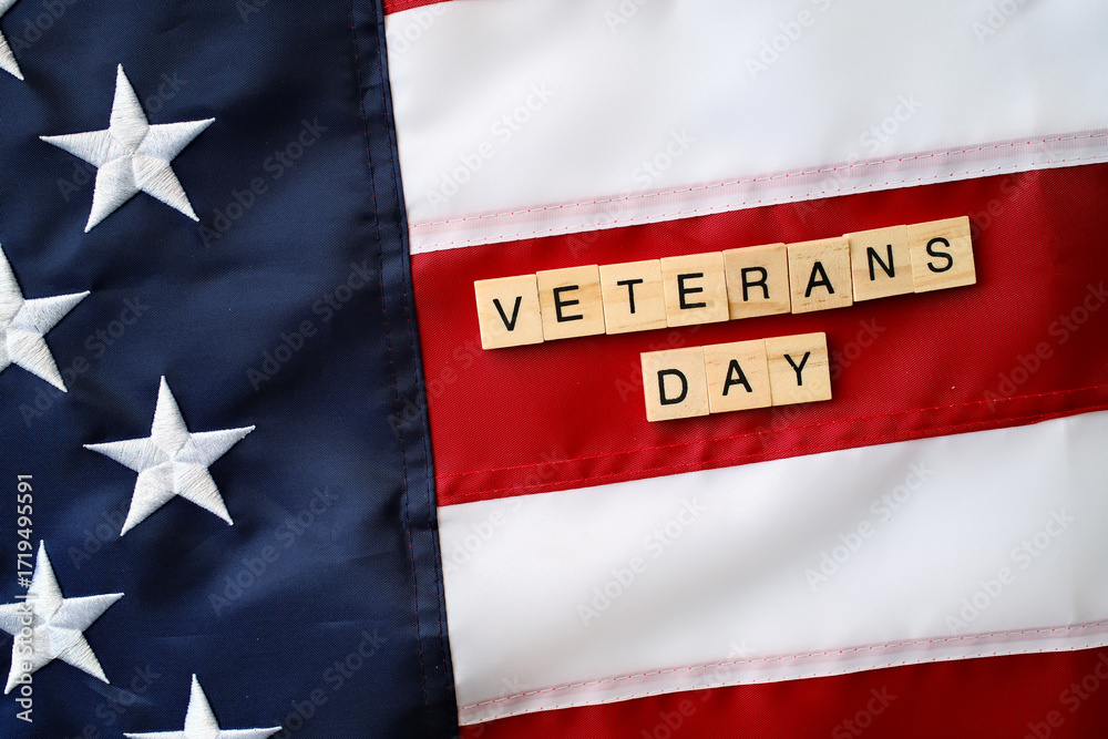 Naklejka premium Veterans Day spelled with wooden letter tiles on American flag, tribute to military service and patriotism
