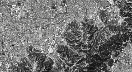 Photo of aerial view of a sprawling city nestled against rugged, mountainous terrain, showcasing urban development and natural landscapes