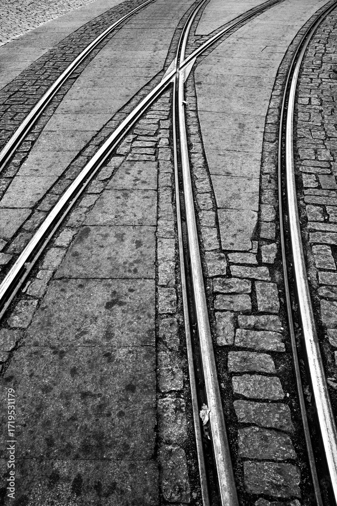Obraz premium Rails of the famous historic tram in Porto (Portugal). Switches and tracks in a curve at the terminus in the old town. Black-and-white infrastructure background with cobblestones. 