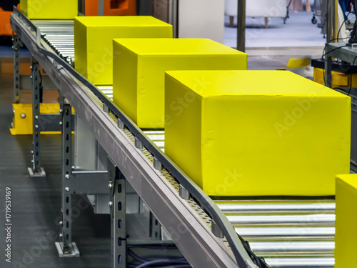 Bright yellow boxes moving along a conveyor belt in a busy warehouse setting