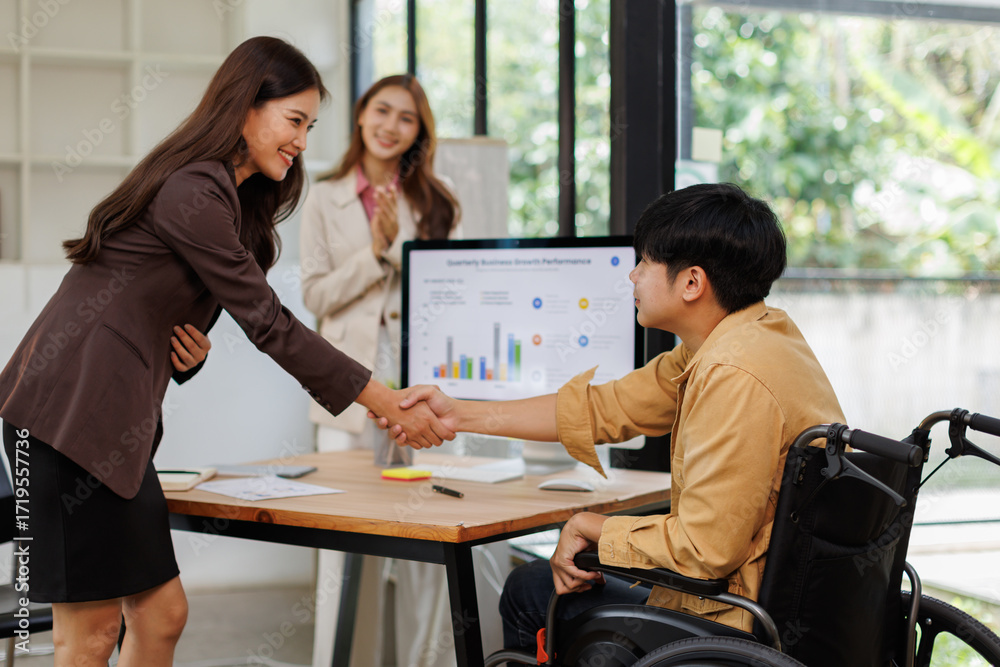 Fototapeta premium Asian businessman sitting on wheelchair shaking hands with asian businesswoman in modern office 
