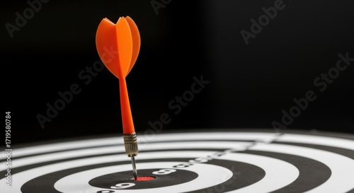 Vibrant Orange Dart Perfectly Striking the Bullseye of a Black-and-White Target, Symbolizing Precision, Focus, and the Achievement of a Strategic Goal Against a Dramatic Dark Background
