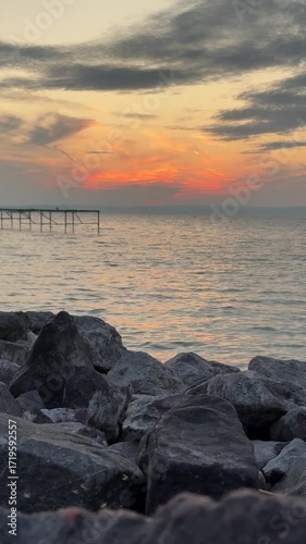 Sunset on the shore of Lake Balaton in Siofok Hungary with rocks and wooden pier vertical