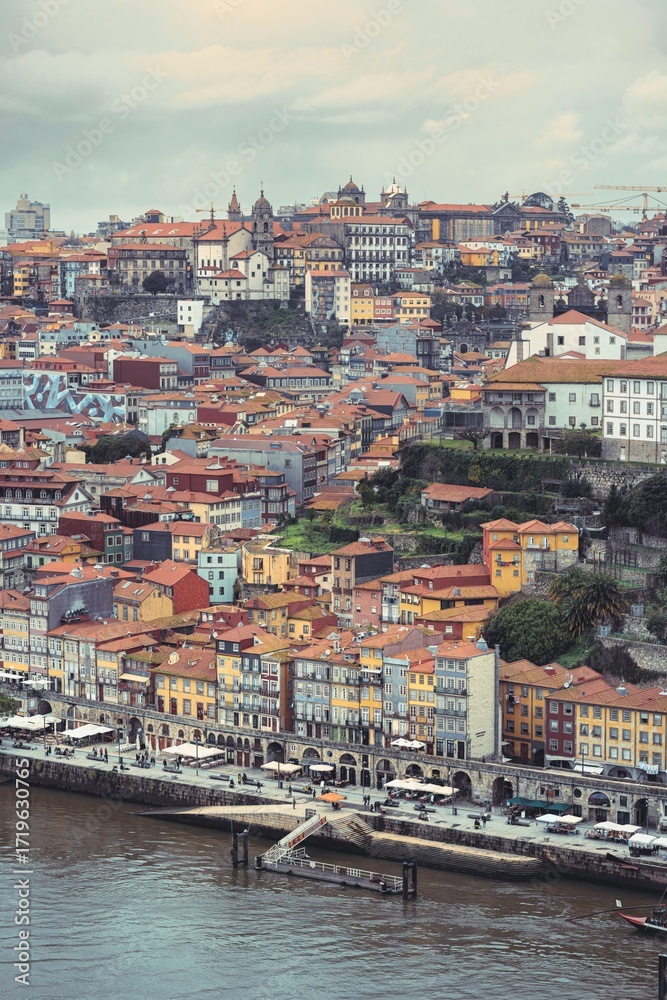 Fototapeta premium A scenic cityscape shows traditional buildings with red tile roofs cascading down a hillside in the Ribeira district of Porto, Portugal on an overcast day