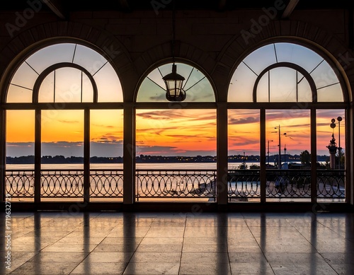 Interior view of arched windows showcasing a vibrant sunset over water