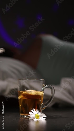 A glass of chamomile tea sits near the bed. Person is lying in bed. A night light provides soft light. Hopefully, it will help with sleep and insomnia.