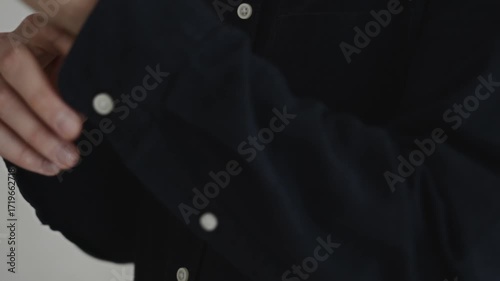 Close-up detail of a buttoned black shirt indoors. The shot emphasizes attention to appearance, professional preparation, and business confidence. High quality 4k footage