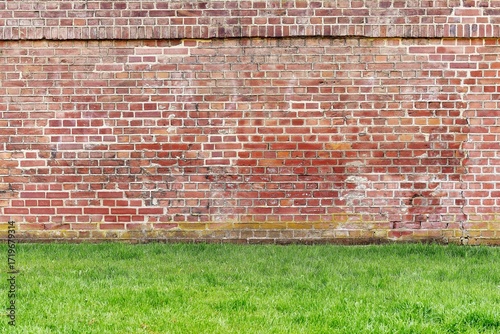 Foto Weathered Red Brick Wall with Green Grass