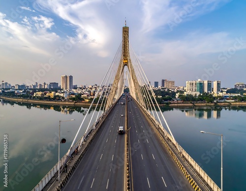 Aerial view of a cable-stayed bridge over a calm river, leading to a city skyline