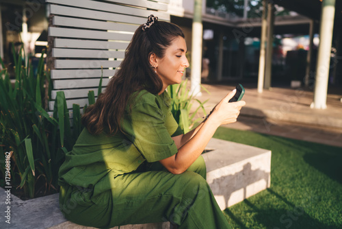 Photography Woman browsing phone with calm smile while seated outdoors, portraying digital mindfulness, solo connection, and intentional screen use in everyday life