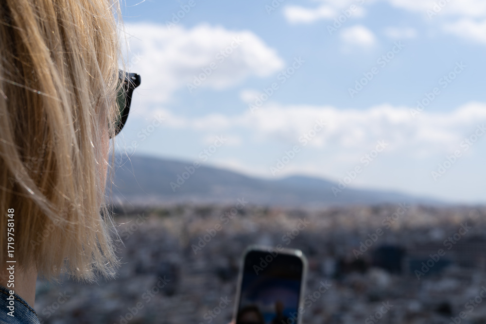 Obraz premium Woman taking photo with smartphone outdoors, tourist capturing city view, blonde female in sunglasses holding phone, travel lifestyle moment.