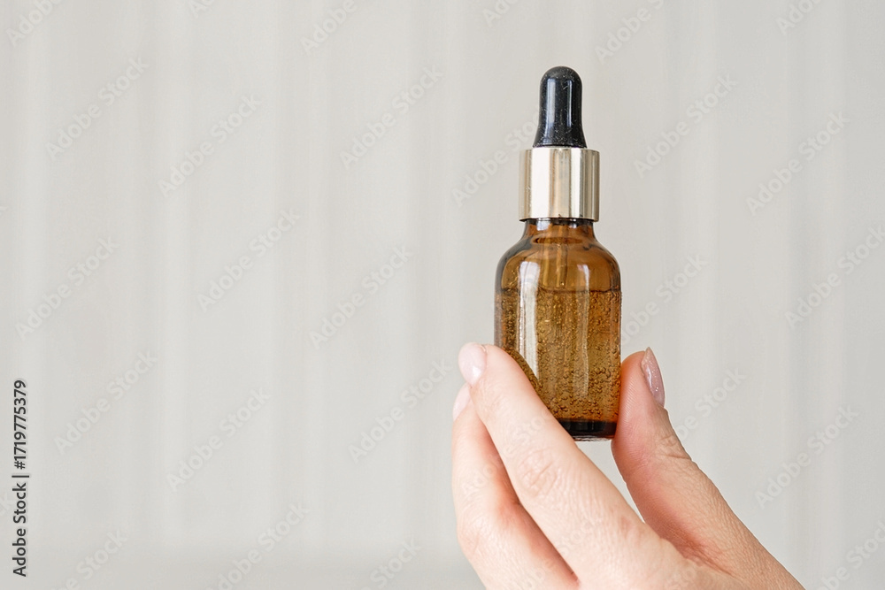 Naklejka premium Female hands showing natural oil cosmetics on a Beige Background. Dropper amber brown glass Bottle with pipette. Spa Beauty products Isolate on Neutral Backdrop. Skincare recommend, makeup advertising