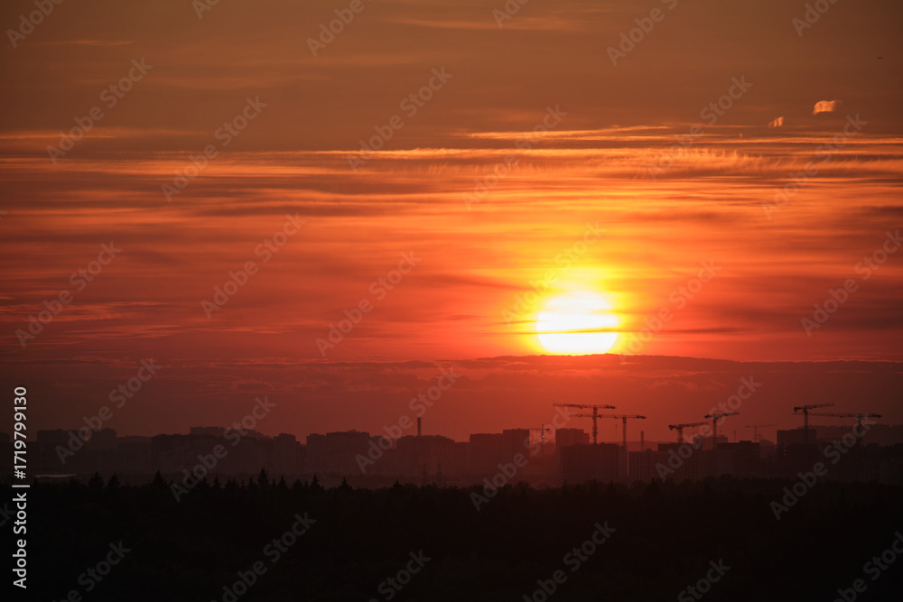 Fototapeta premium Silhouetted city skyline with construction cranes under a vivid orange sunset, capturing urban development and natural beauty together.