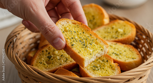 A hand picking up a slice of garlic bread from a basket