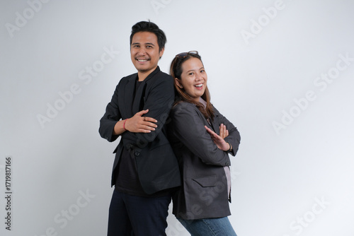Smiling man and woman in formal attire standing back to back with crossed arms. Studio portrait on plain background representing teamwork.