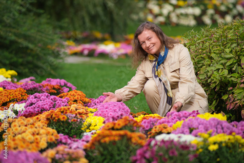 Woman admiring colorful chrysanthemum flower. Happy caucasian female enjoying autumn garden. Gardening hobby and outdoor activity concept. Middle-aged woman (50 years old)