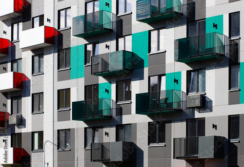 Facade of a contemporary apartment building with modern balconies, turquoise, gray, black, and red