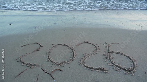 This video captures the year '2026' elegantly drawn on a sandy beach, symbolising aspirations, the passage of time and waves on the beach wash away the inscription