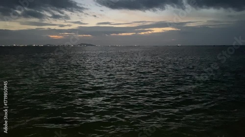 Serene Twilight Over Calm Ocean Waters with Distant Lights and Cloudy Skies
