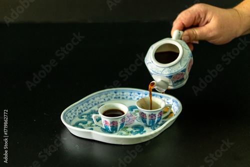 A person is pouring coffee into two cups from a teapot
