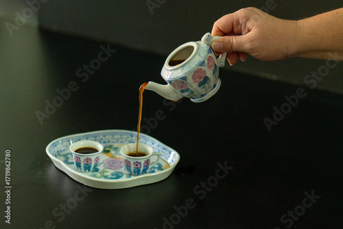 A person is pouring coffee into a teapot from a small cup
