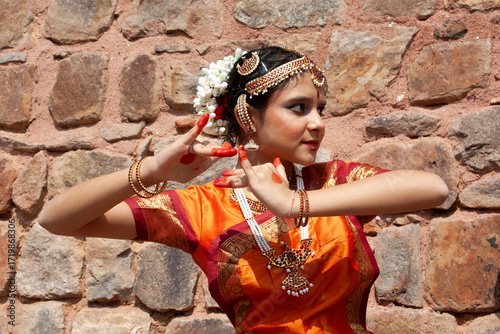 Teenage girl in traditional clothing with alta dye on her hands and feet standing by a building performing an Indian Bharatnatyam dance, New Delhi, India