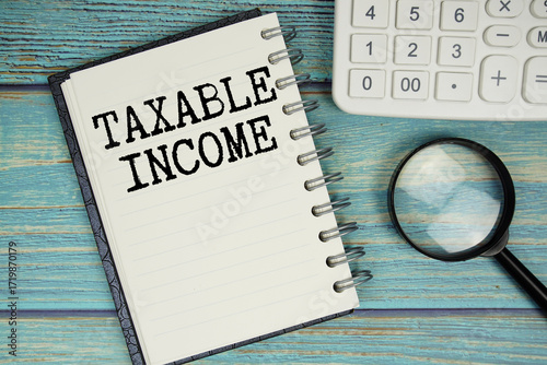 Taxable Income text on notepad with magnifying glass and calculator on wooden background