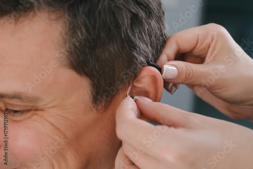 Man trying modern compact hearing aids. Closeup of patient ear. Hearing rehabilitation clinic selecting digital device for middle age deaf people. Close-up